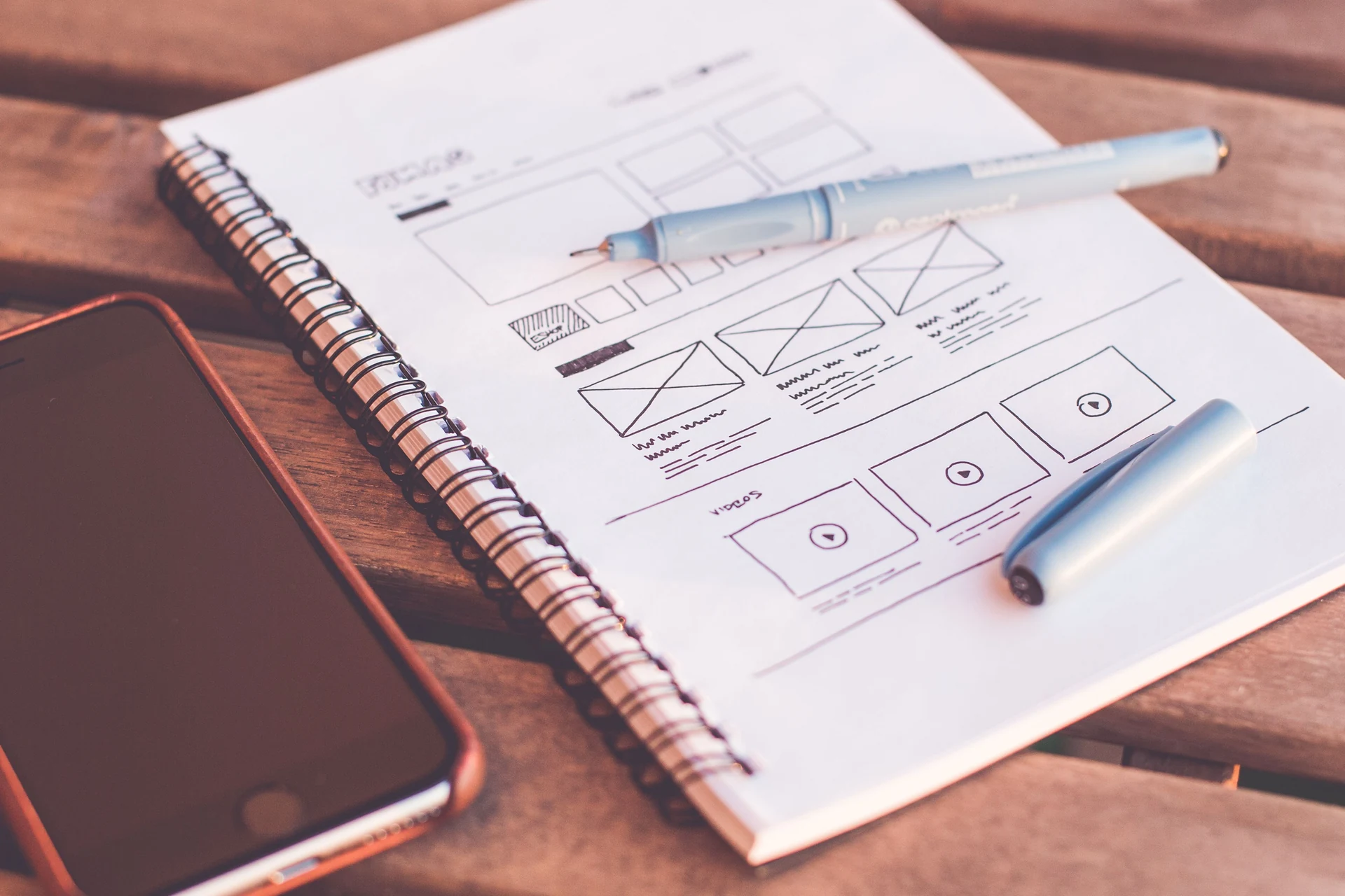Des croquis de pages web dans un carnet, à côté d’un téléphone et de stylos.